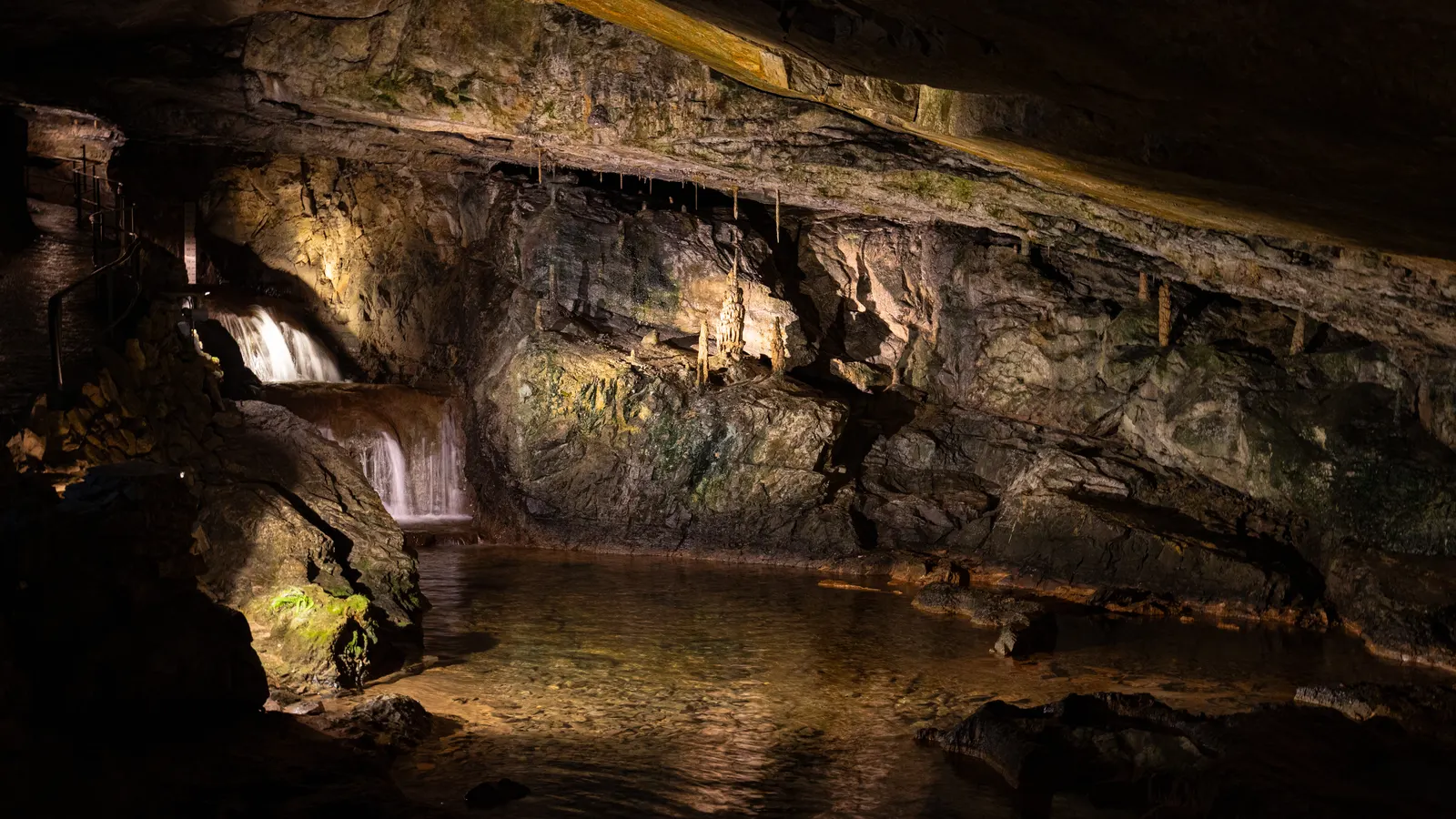 A broad chamber in the St Beatus Caves with the stream running through it and the rock wall lit from the side