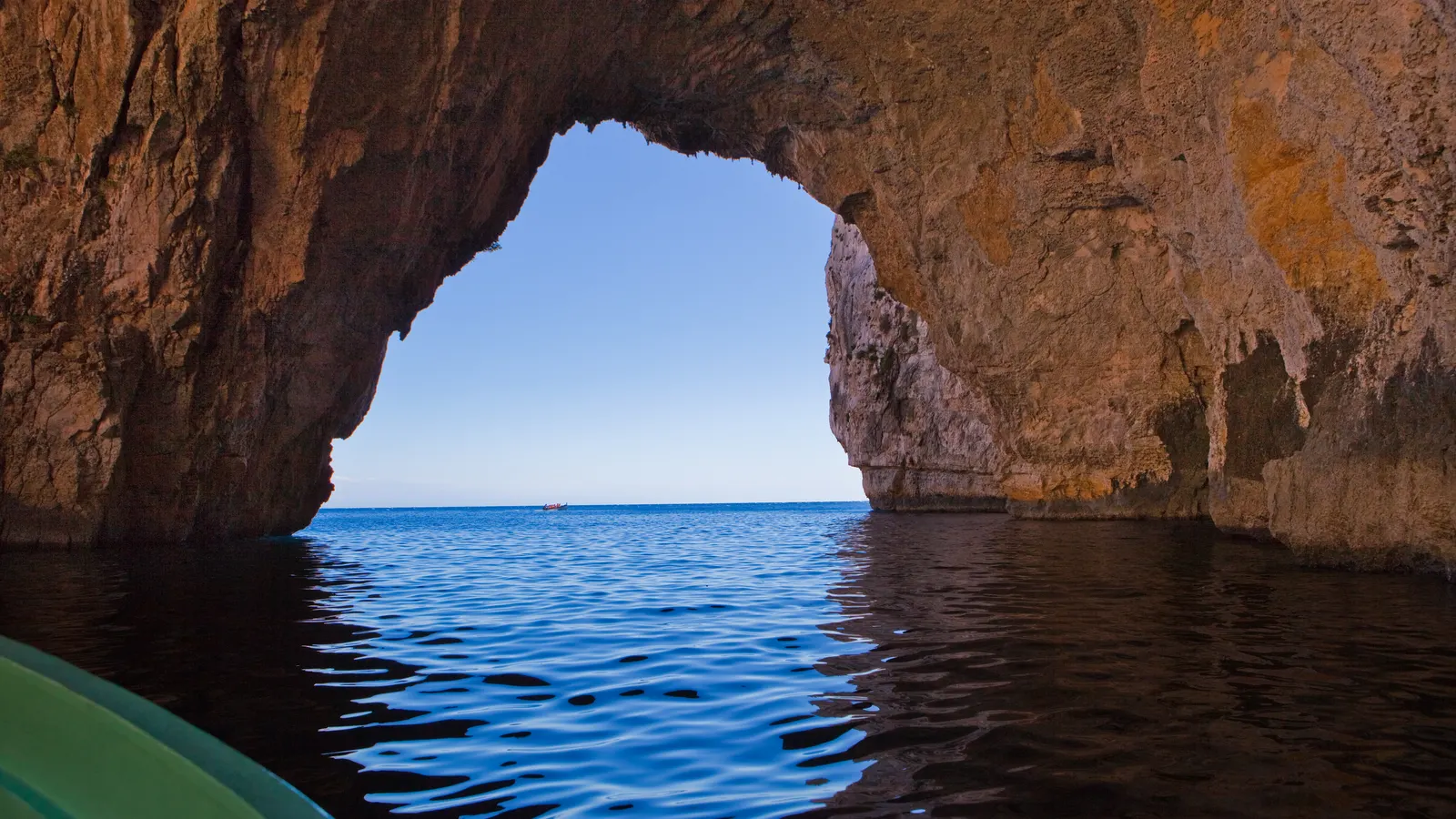 View from a small boat through the rock arch of the Blue Grotto in Malta onto calm, deep blue sea