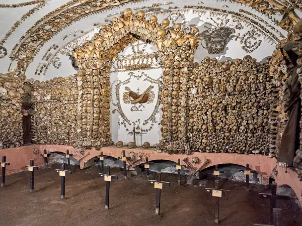 Walls of stacked bones above earthen graves marked with small crosses in a chapel of the Capuchin Crypt in Rome.