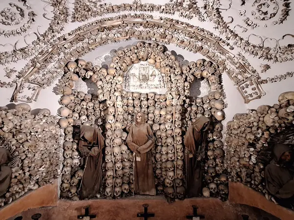 Robed friars stand in niches of stacked skulls in the Crypt of the Skulls, one of the bone chapels of the Capuchin Crypt in Rome.