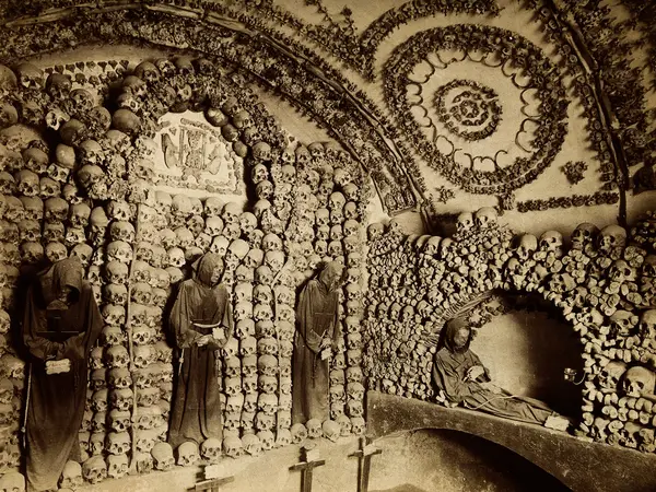 Historic photograph of robed friars among arches and columns of skulls in the Capuchin Crypt beneath the church on Via Veneto.