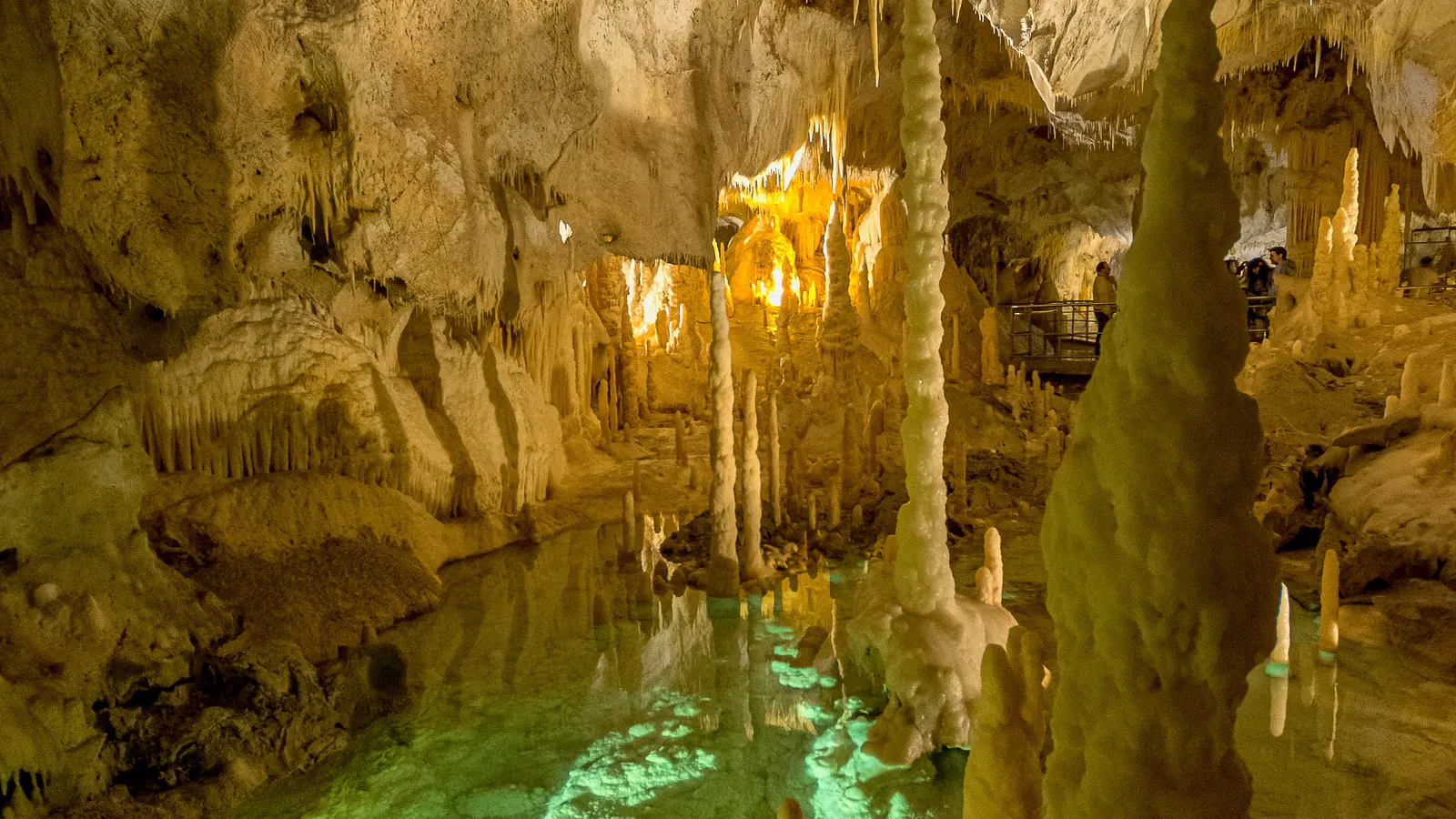 A lit chamber in the Frasassi caves, with stalagmites standing over still water