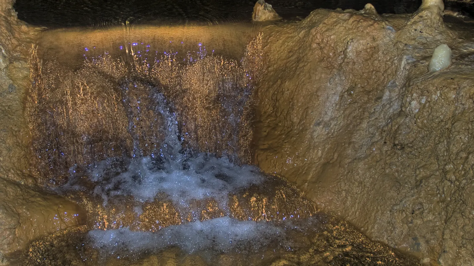 A lit waterfall spilling over golden flowstone pools in Harrison's Cave, Barbados