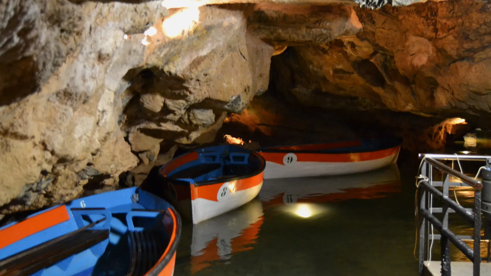 Boats at the landing stage inside the Caves of Sant Josep, lit rock walls above the water