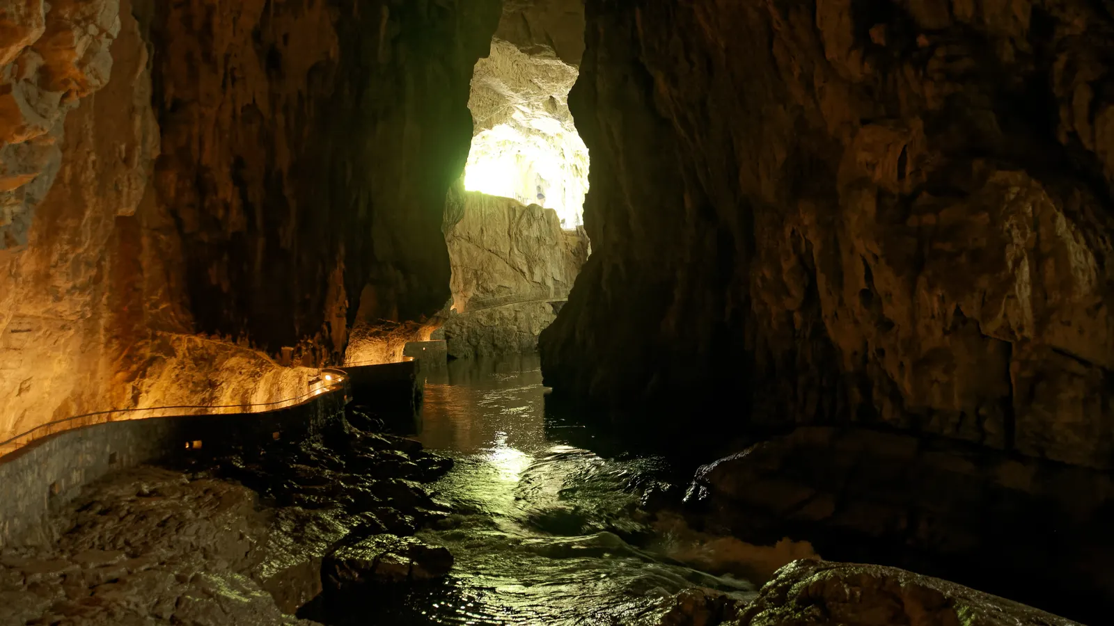Daylight falling through an opening in the rock onto the path beside the Reka in the Škocjan Caves