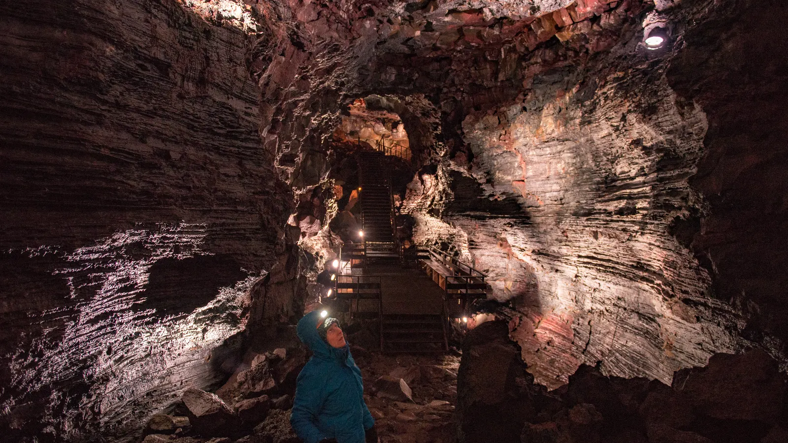 Lit walkway through the red-brown lava tunnel Raufarhólshellir in Iceland, one person in the passage