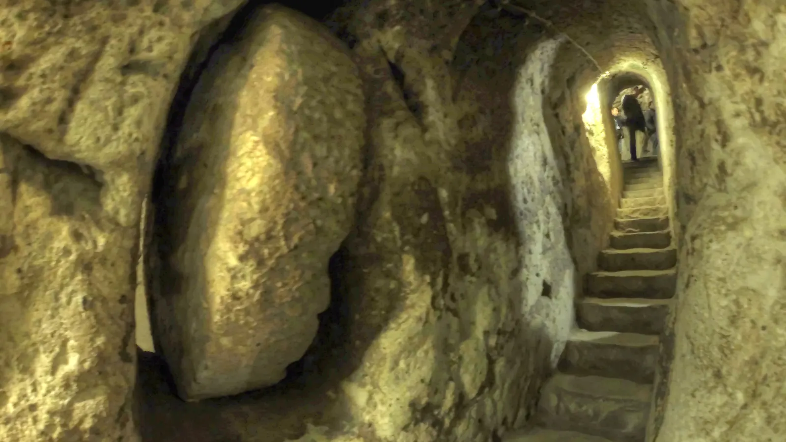 A round rolling stone door beside a narrow staircase in the underground city of Derinkuyu
