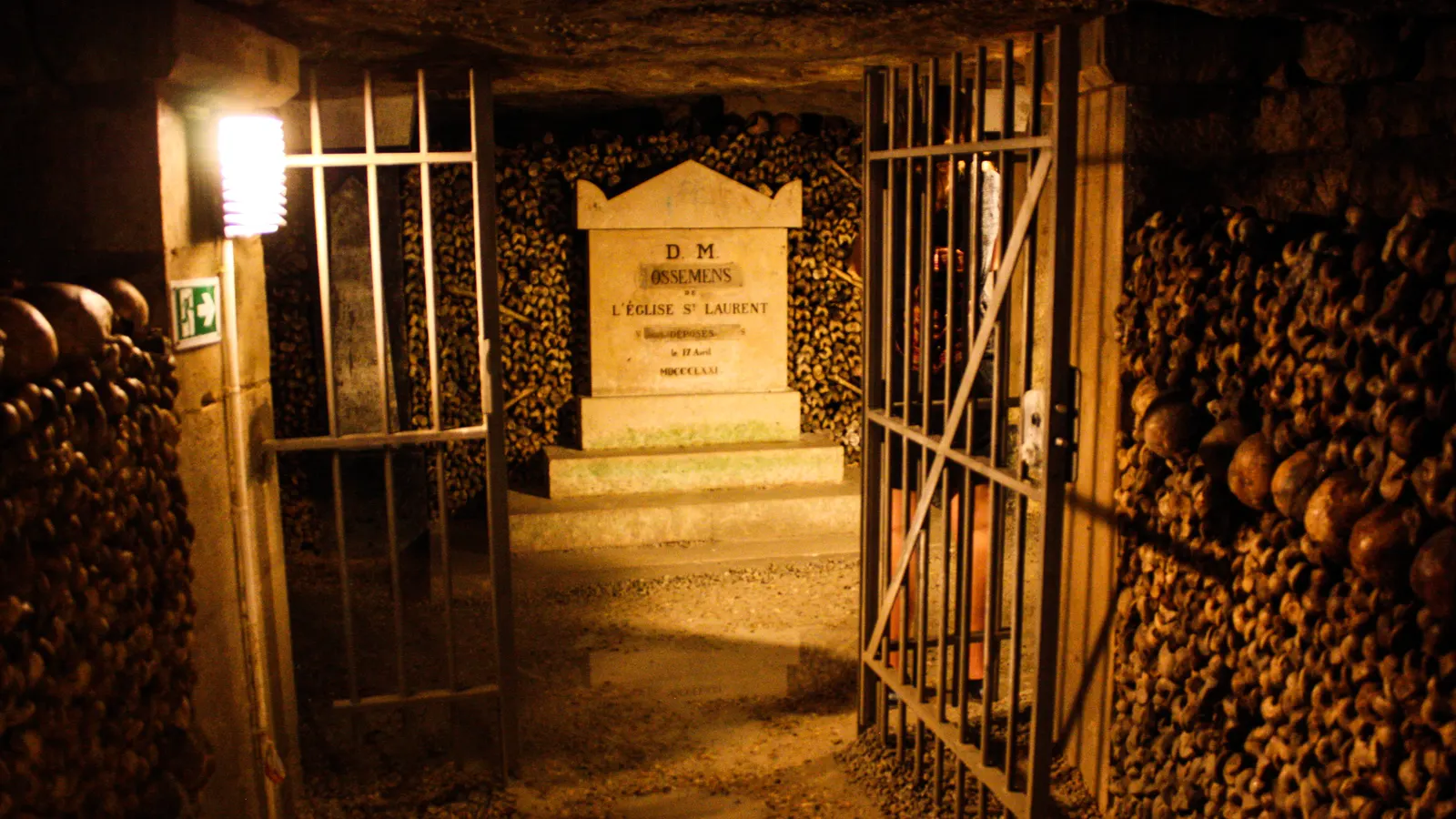 An open iron gate in the ossuary of the Paris catacombs, walls of skulls and bones behind it