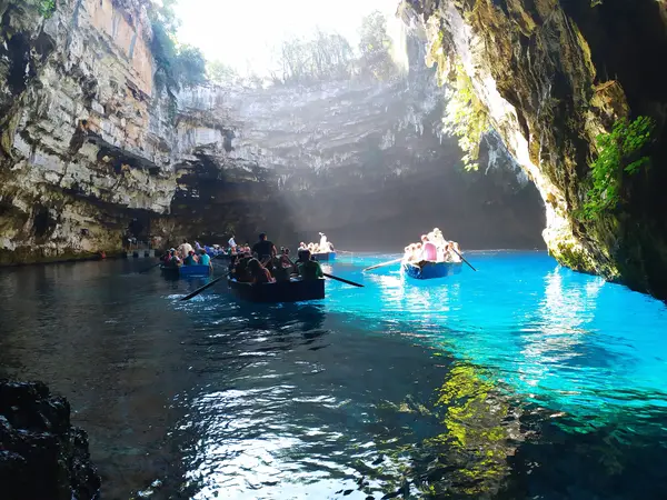 Several tour boats float on the turquoise lake beneath the overhanging limestone walls of Melissani Cave.