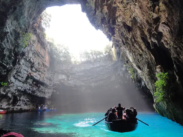 Sunlight pours through the collapsed roof of Melissani Cave onto a rowing boat crossing the underground lake.