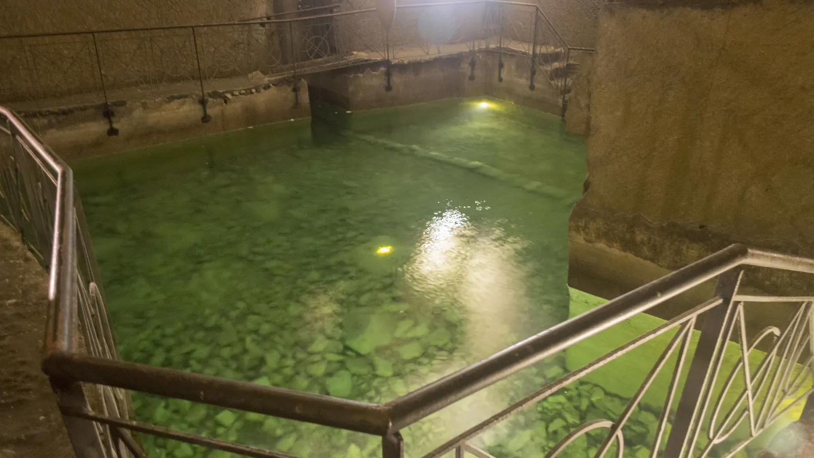 A green-lit cistern with a railing in the underground of Naples